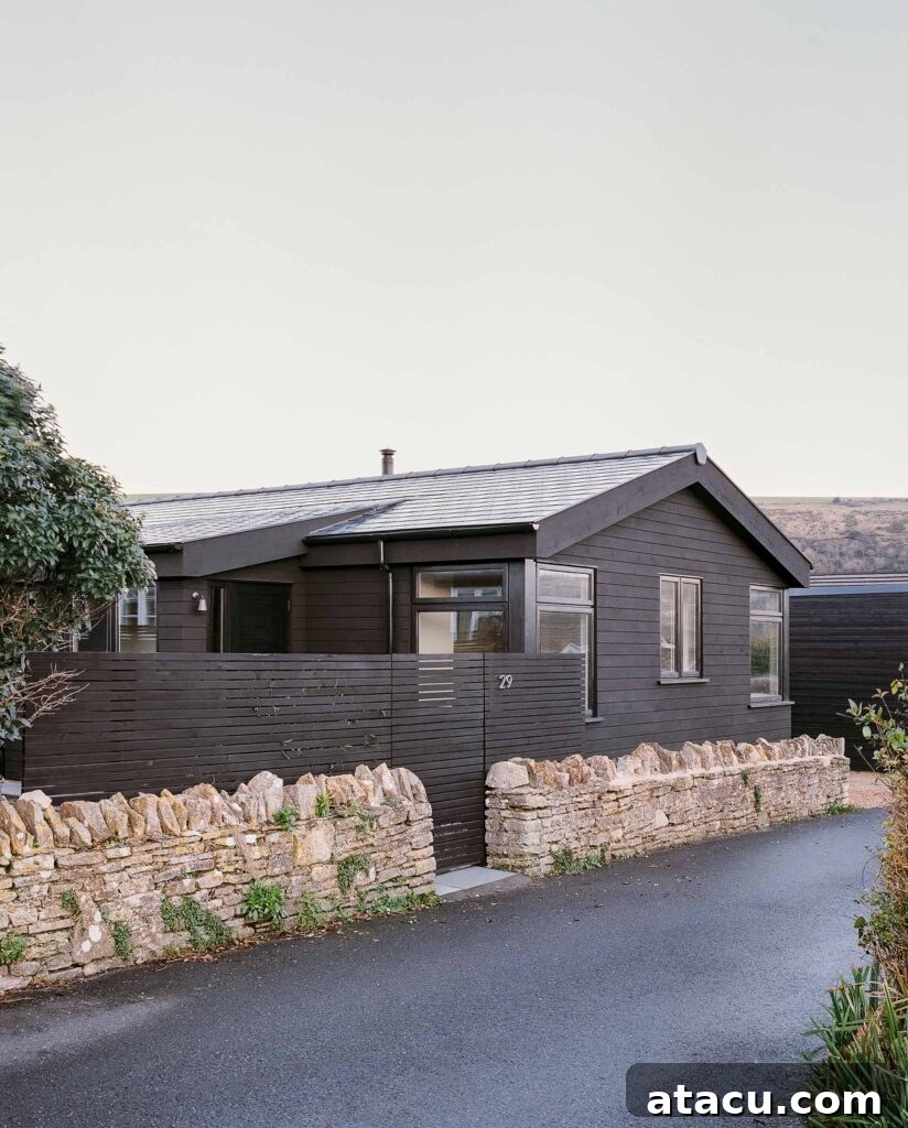 Modern black wood cabin with stone wall and pitched roof.