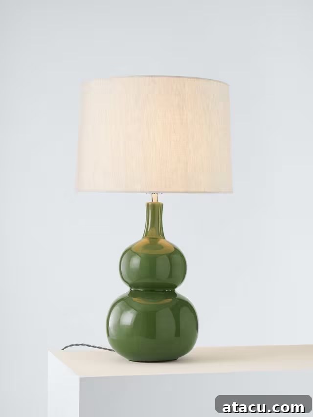 A stylish green ceramic sculptural table lamp with a natural linen drum shade, perfect for ambient lighting.