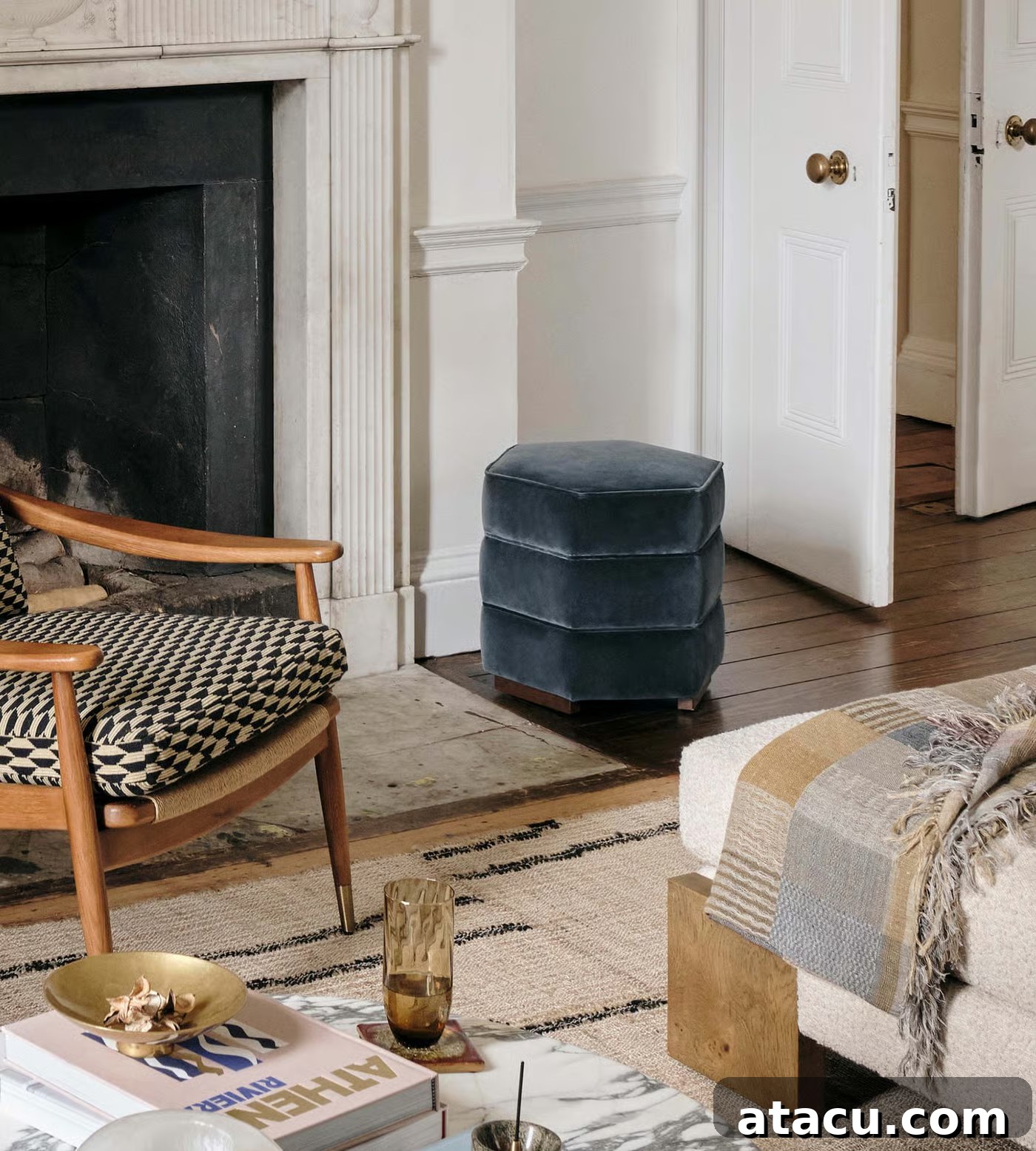 An elegant living room setting featuring a luxurious blue velvet footstool positioned in front of a classic marble fireplace, offering both style and flexible functionality.
