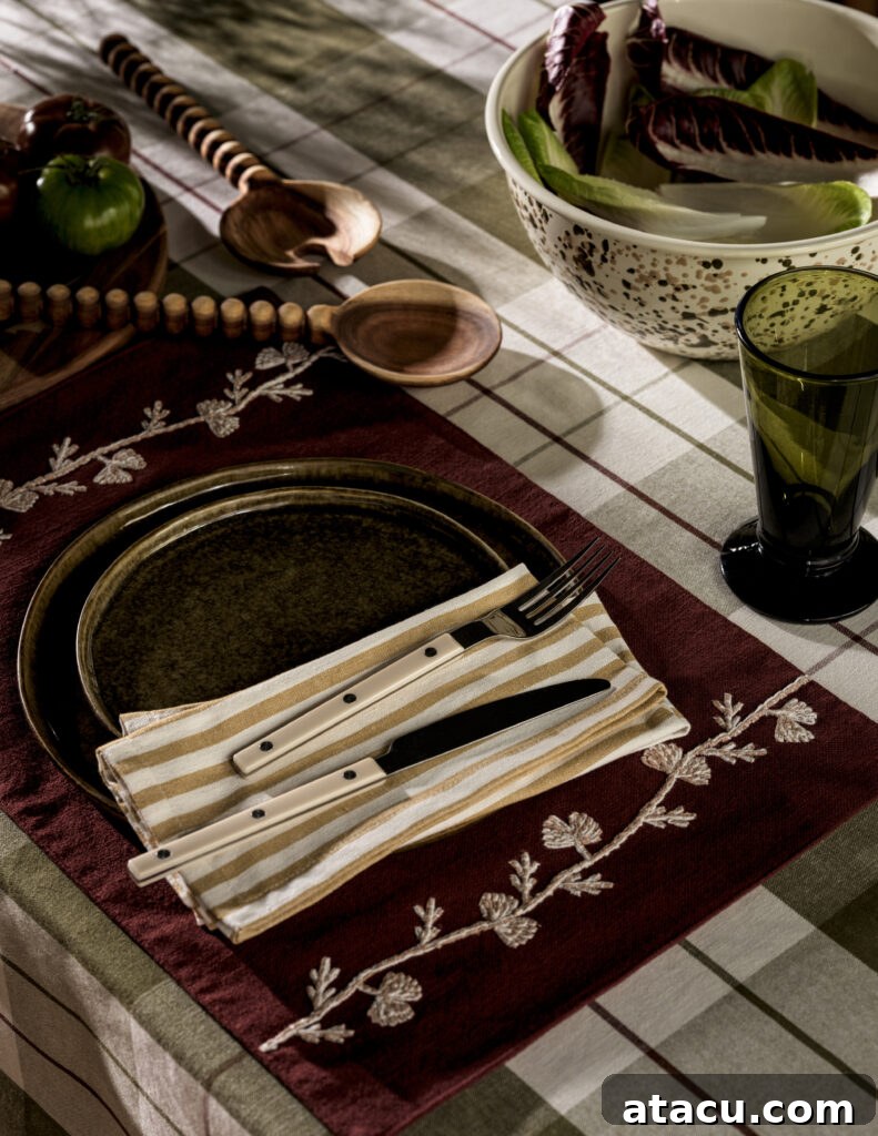 Rustic table setting with embroidered placemat, striped napkin, and wooden utensils.
