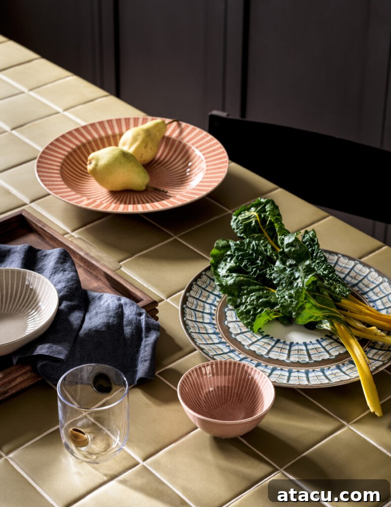 Tiled kitchen counter with ceramic tableware, pears, and fresh leafy greens.