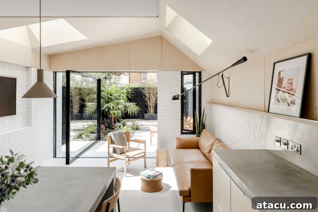 Expansive open-plan kitchen and living area featuring a neutral color palette, a comfortable leather sofa, and large sliding glass doors that open to a beautifully landscaped garden.