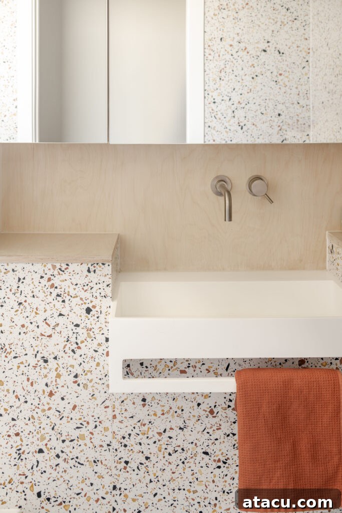 A modern bathroom sink setup featuring stylish terrazzo tiles, a warm wood backsplash, and an inviting rust-coloured hand towel, adding a splash of vibrant color.