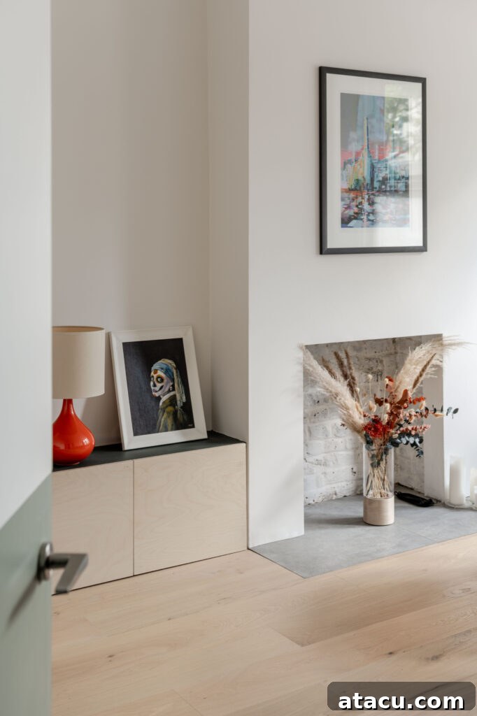 A minimalist living room corner adorned with modern abstract art, a vibrant red lamp, and an elegant dried floral arrangement, all set within a serene white-walled interior.