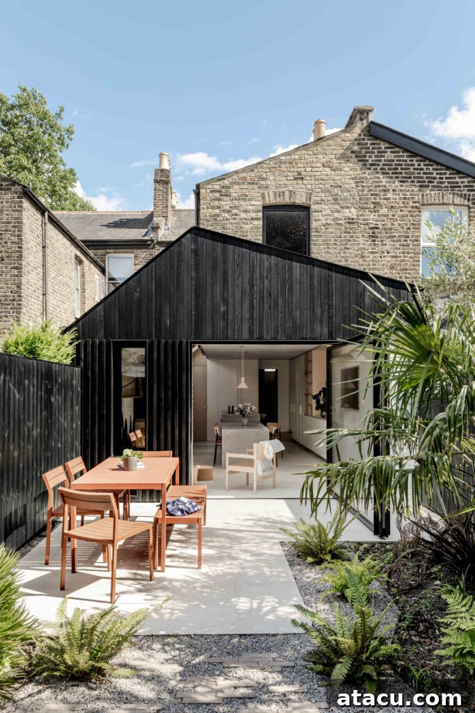 A contemporary black timber house extension opening onto a minimalist outdoor dining area, thoughtfully integrated within a lush, natural garden setting.