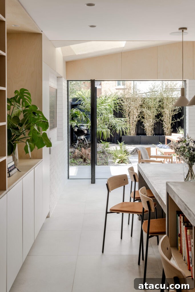 A modern kitchen featuring a concrete dining island and stylish wooden chairs, with expansive glass doors offering a picturesque view of the garden, creating a perfect blend of indoor and outdoor living.