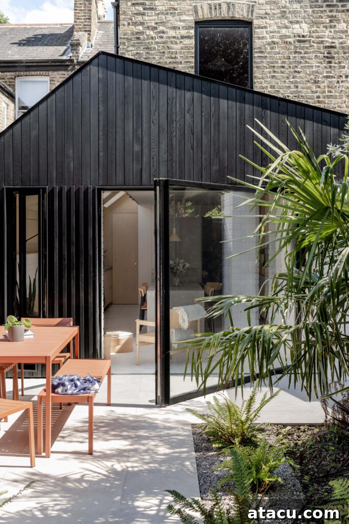A striking black timber-clad extension featuring large pivoting glass doors that open generously to a meticulously landscaped patio garden, blending modern design with natural surroundings.