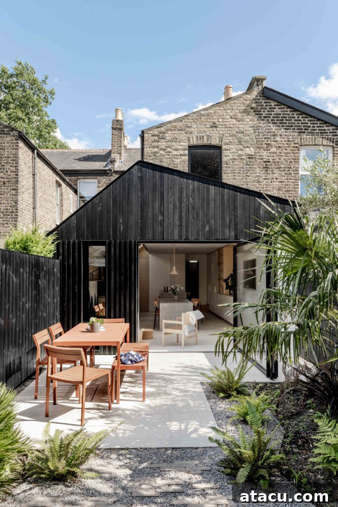 A striking modern black-clad house extension featuring an inviting outdoor dining area and thoughtful garden landscaping, creating a perfect space for al fresco living.
