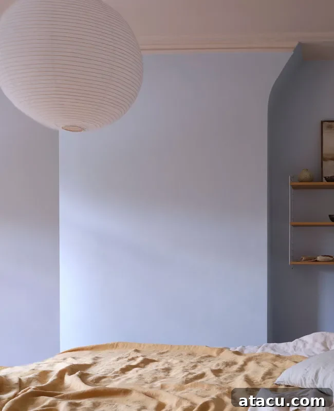 Soft blue bedroom walls painted in Farrow & Ball’s Kakelugn, with a paper lantern and mustard bedding.
