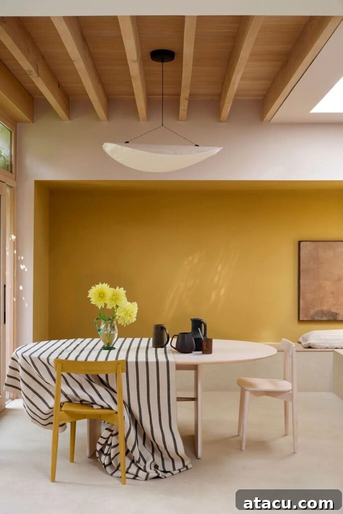 A modern dining space featuring a warm ochre accent wall painted in a new Farrow & Ball colour, complemented by natural wood beams, minimalist furniture, and a striped linen tablecloth.