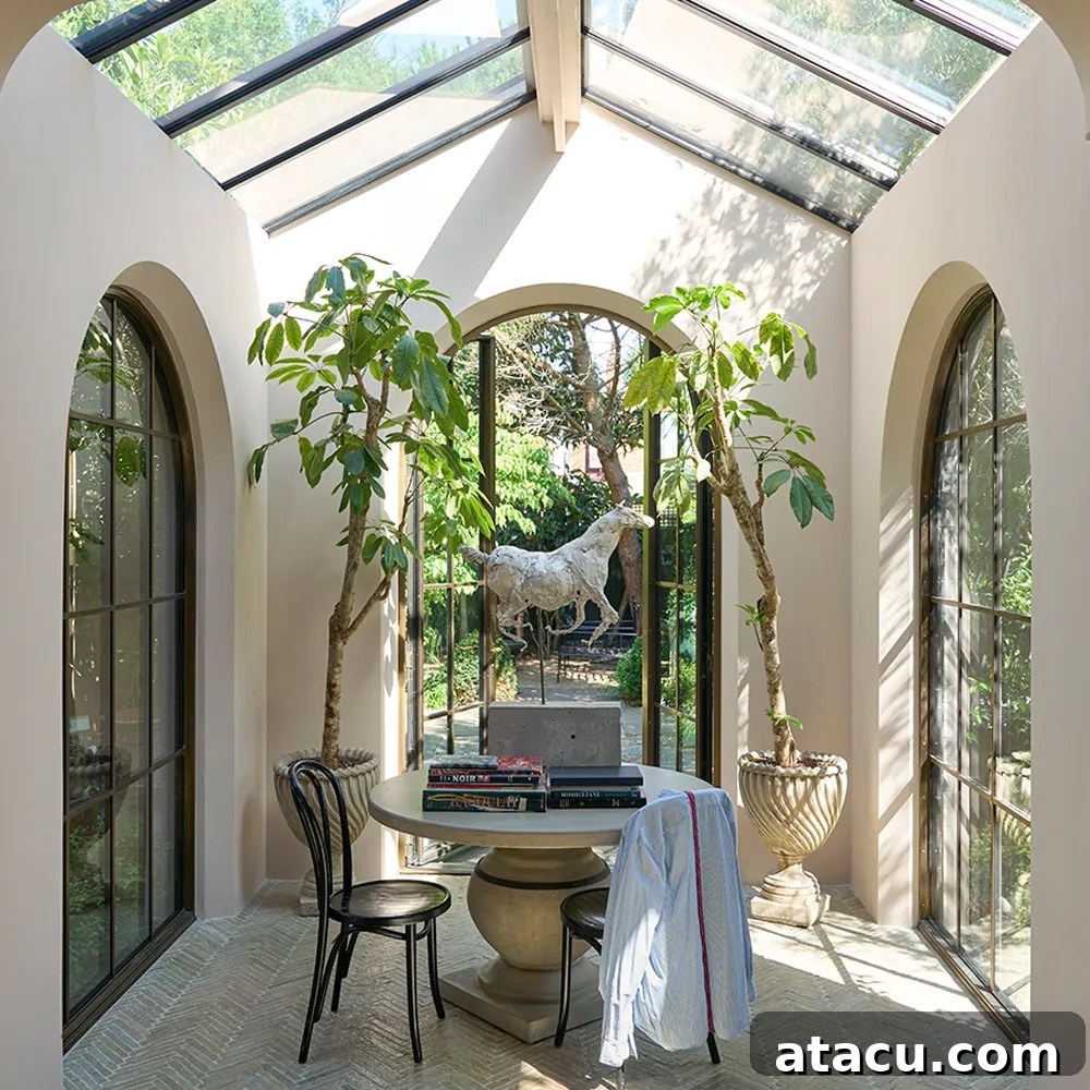 Sunlit conservatory with walls painted in Scallop by Farrow & Ball, arched windows, and a round stone table.