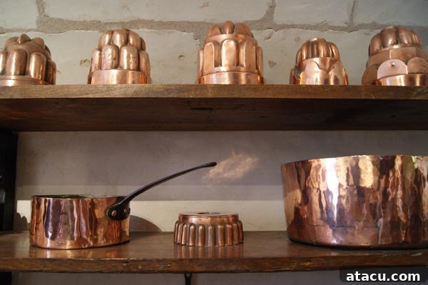 Numerous gleaming copper pots and pans hanging neatly, showcasing the impressive kitchenware collection at Chenonceau.