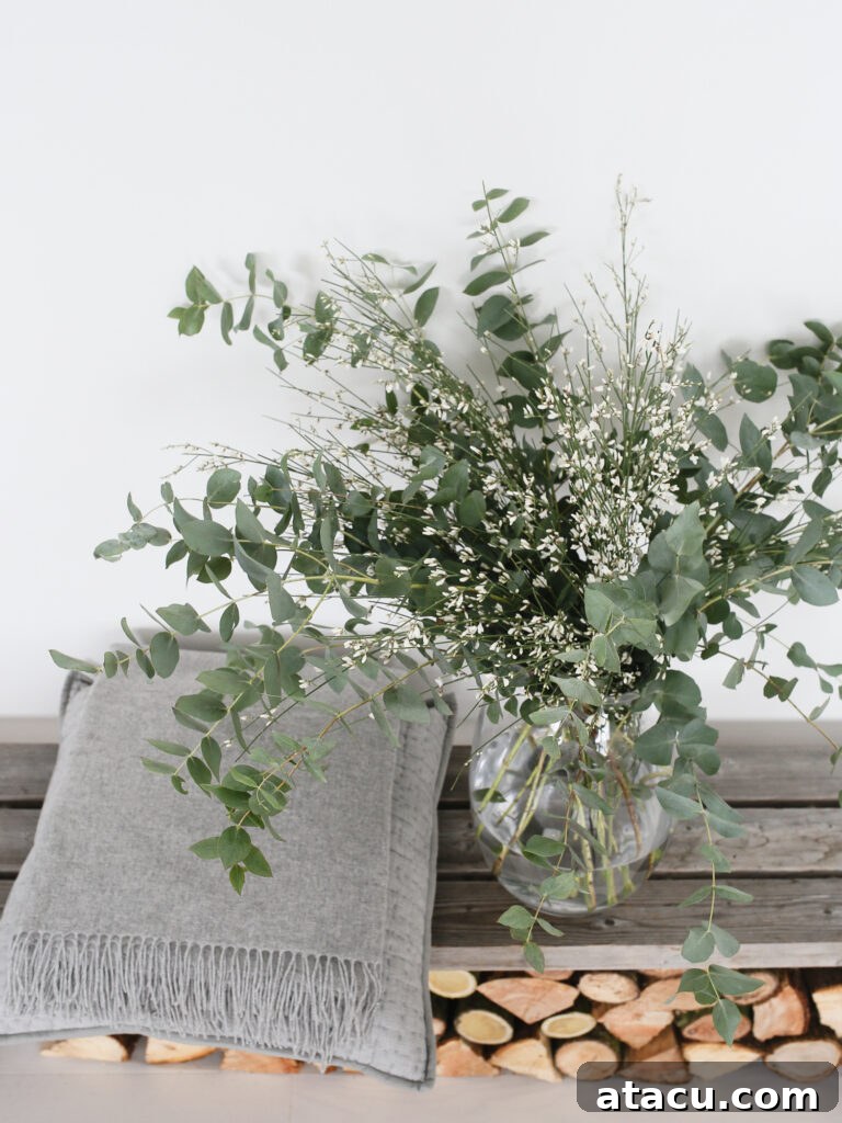 A simple, clear glass vase holding a delicate arrangement of green foliage and white flowers, contributing to a serene interior.