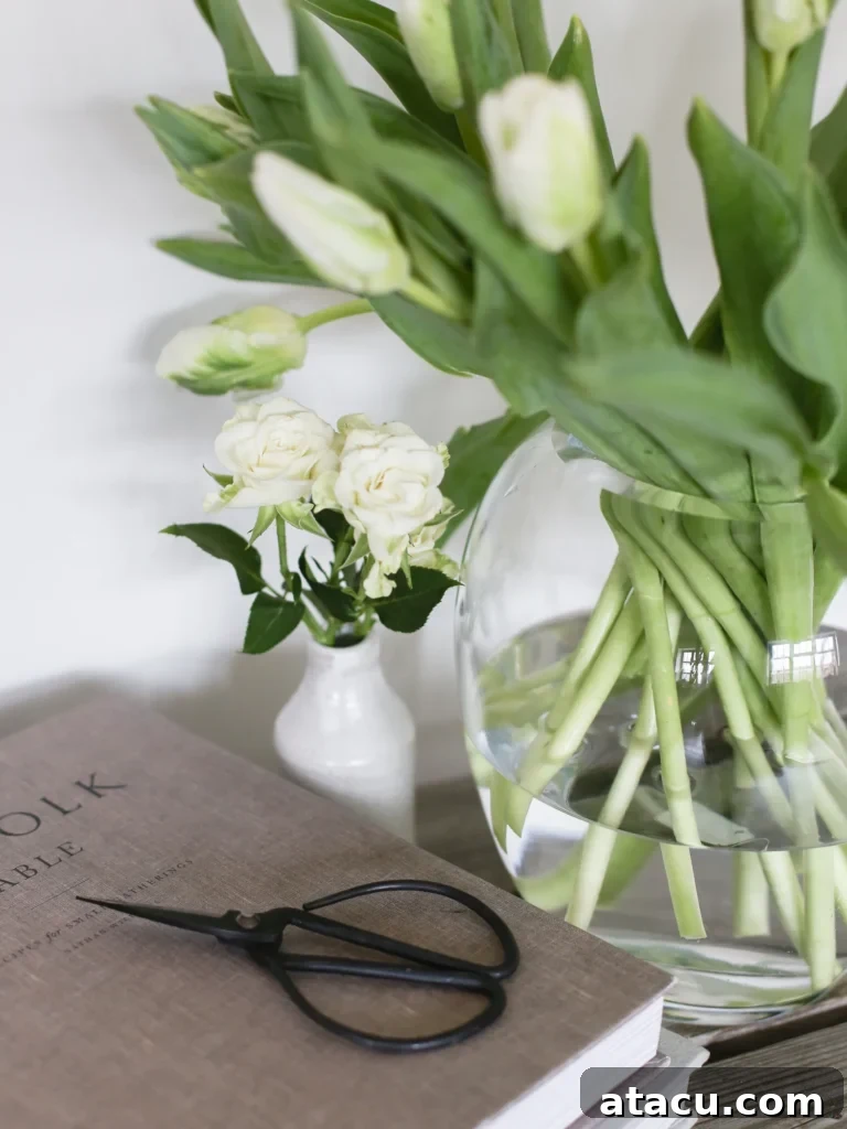 An oval-shaped glass vase filled with a vibrant bouquet of pink tulips and green foliage, placed on a light surface.