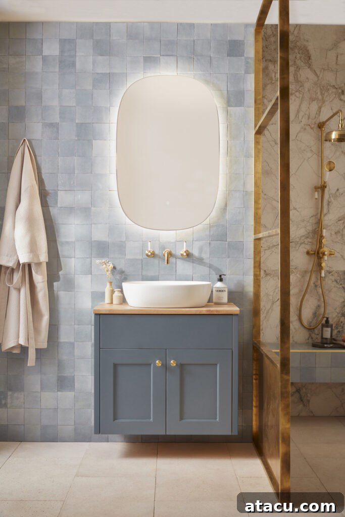 Modern bathroom featuring the Burford Basin Unit in Dusk Blue by Roper Rhodes. The unit includes a sleek white countertop basin, soft blue cabinetry with gold handles, and a wooden top, set against a blue tiled wall and marble shower area with brass fixtures.